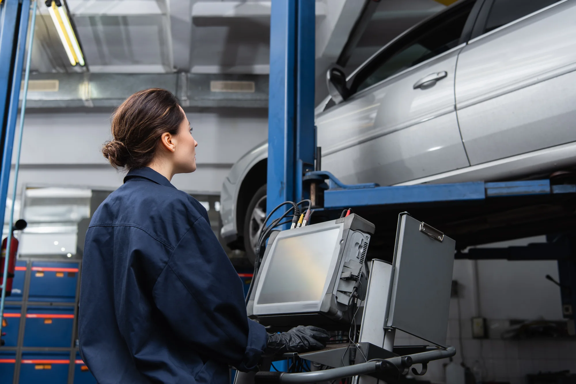 Automotive technician using diagnostic equipment beside a vehicle